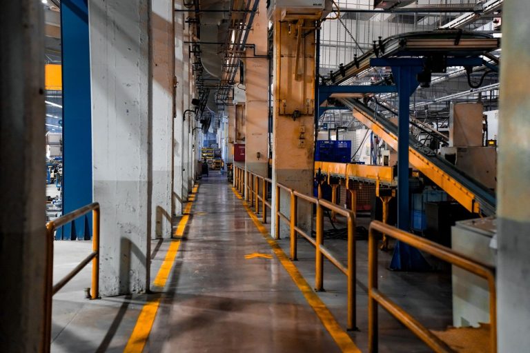 Interior de uma fábrica moderna com máquinas industriais e sistemas de esteiras transportadoras.